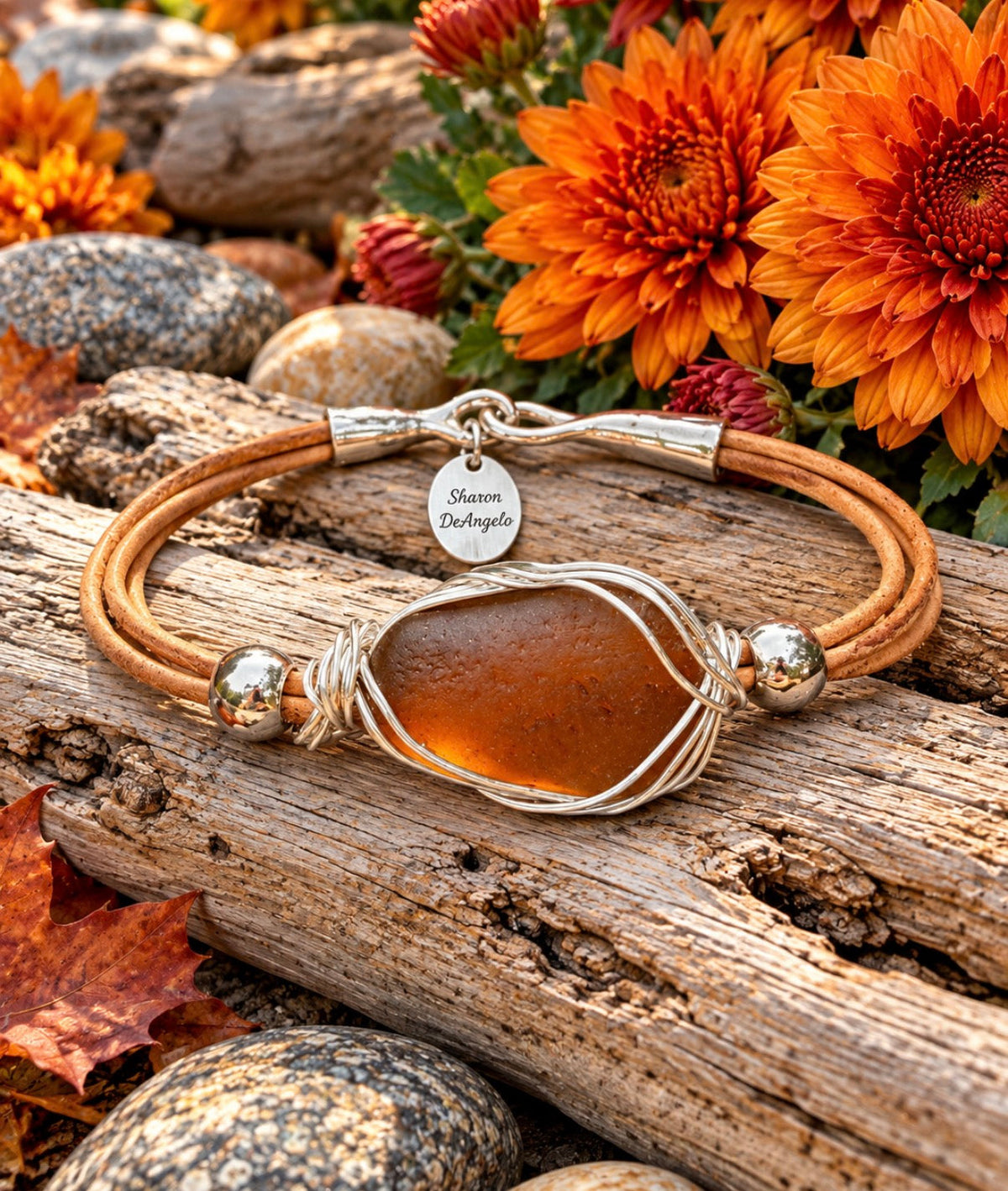 Amber sea-glass leather bracelet wrapped in sterling silver, photographed on driftwood among autumn flowers