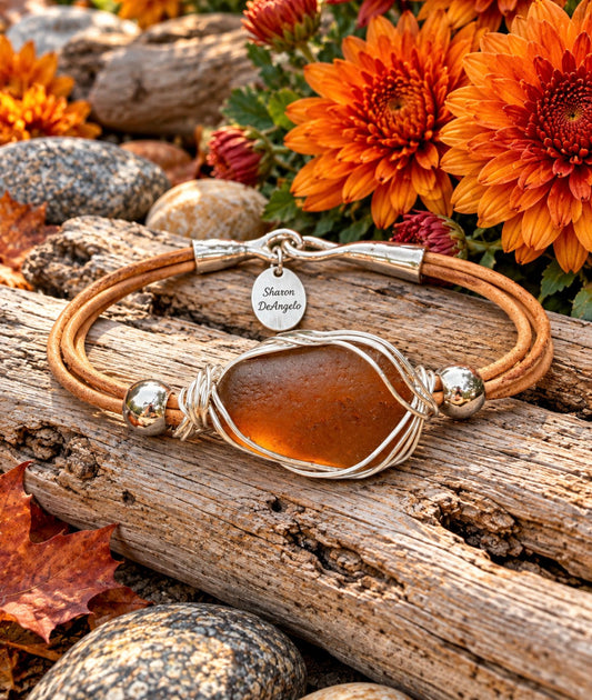 Amber sea-glass leather bracelet wrapped in sterling silver, photographed on driftwood among autumn flowers