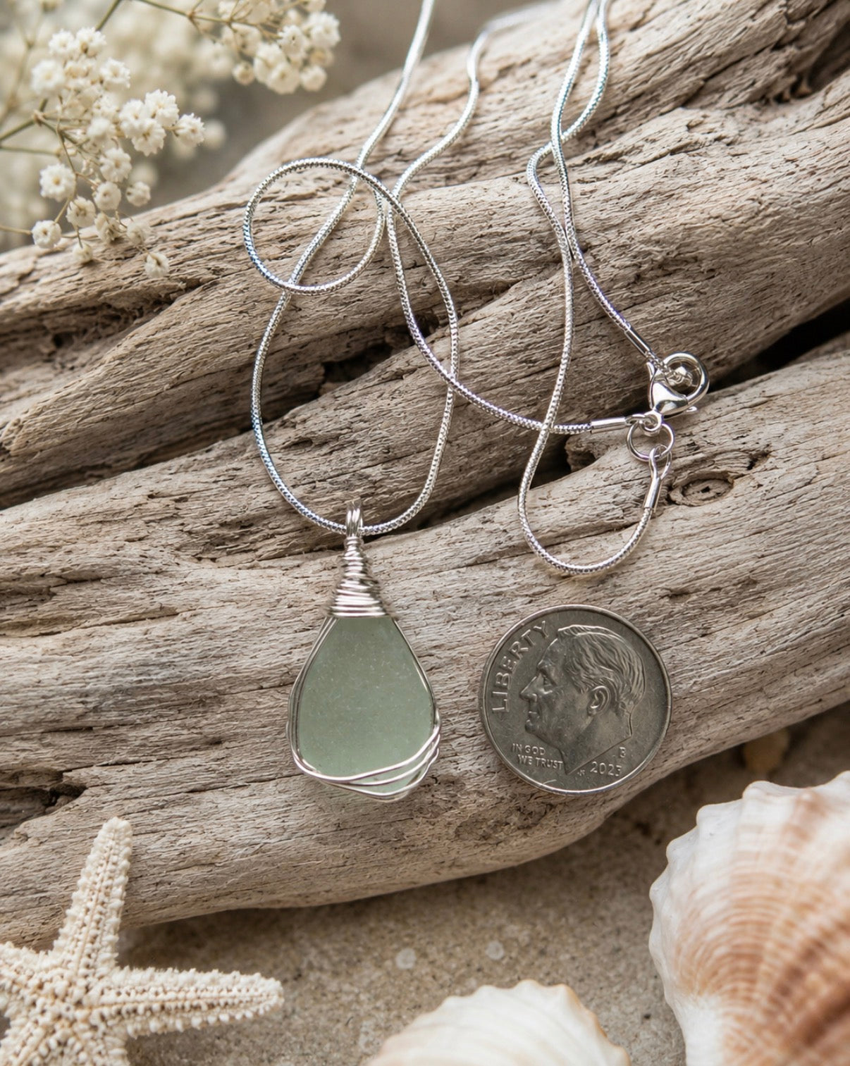 Cola green sea glass pendant wire wrapped in sterling silver, shown next to a dime for scale on driftwood